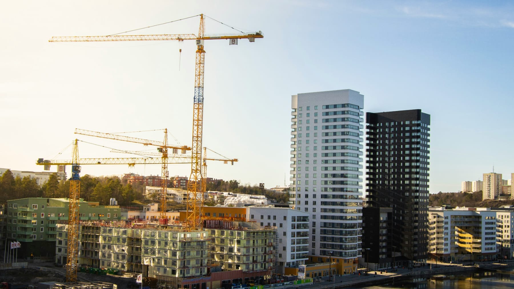 Een bouwplaats met kraan en flatgebouwen in aanbouw, naast flatgebouwen die al gereed zijn